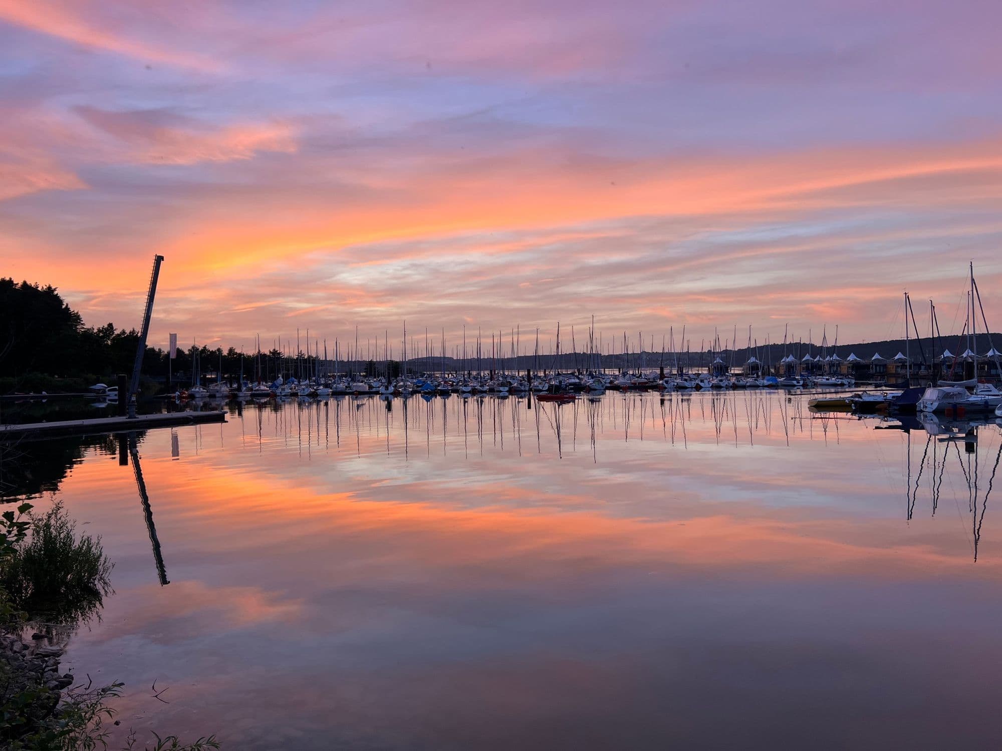 Sailing boats in the marina reflected in the still lake under a pink sky