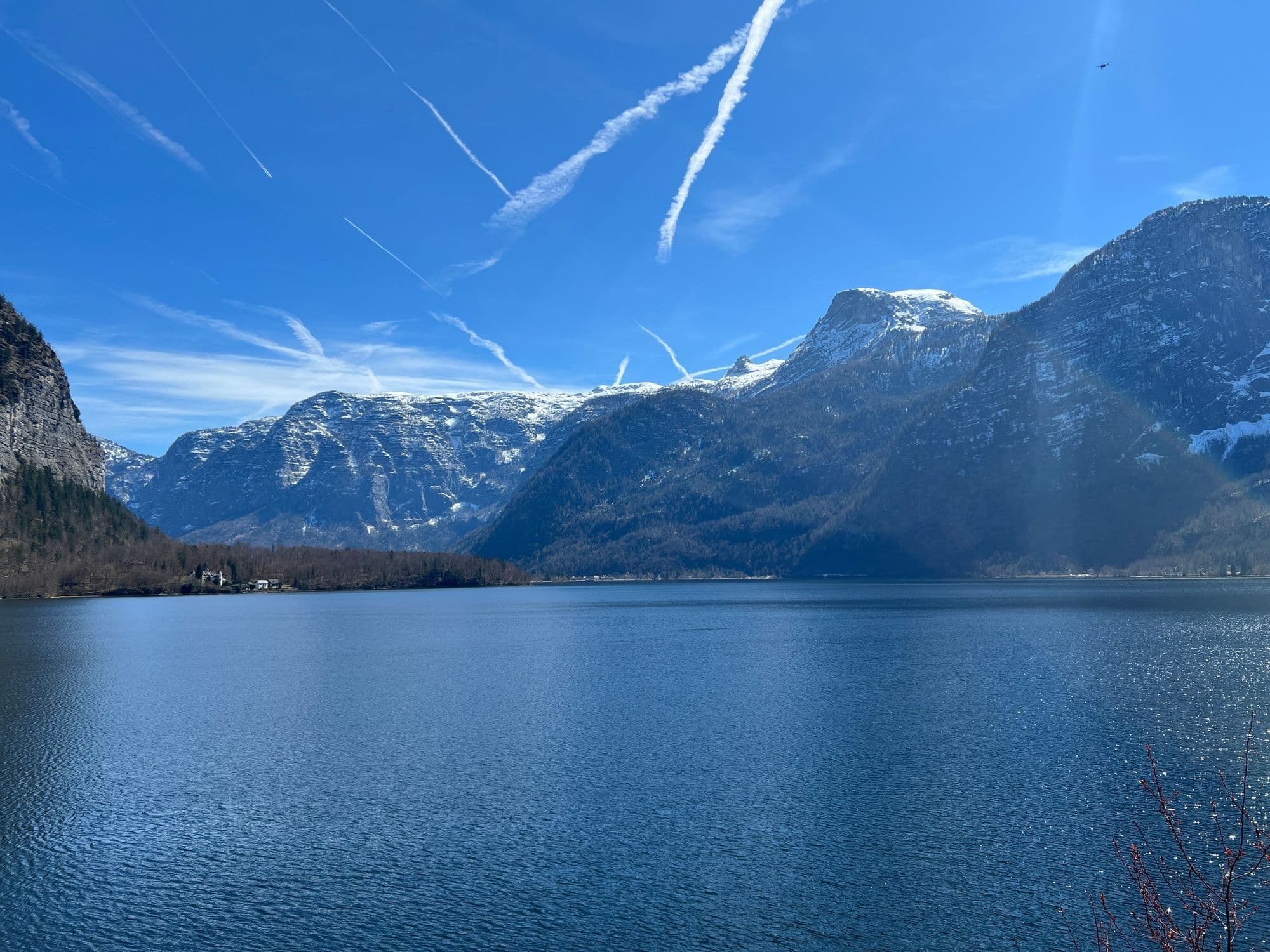 Lake Hallstatt with snowy mountains and contrails in a blue sky