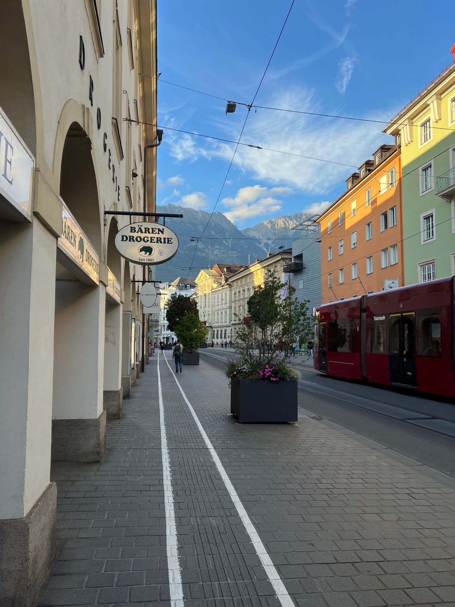 Arcaded street with a red tram and mountains at the end of the road