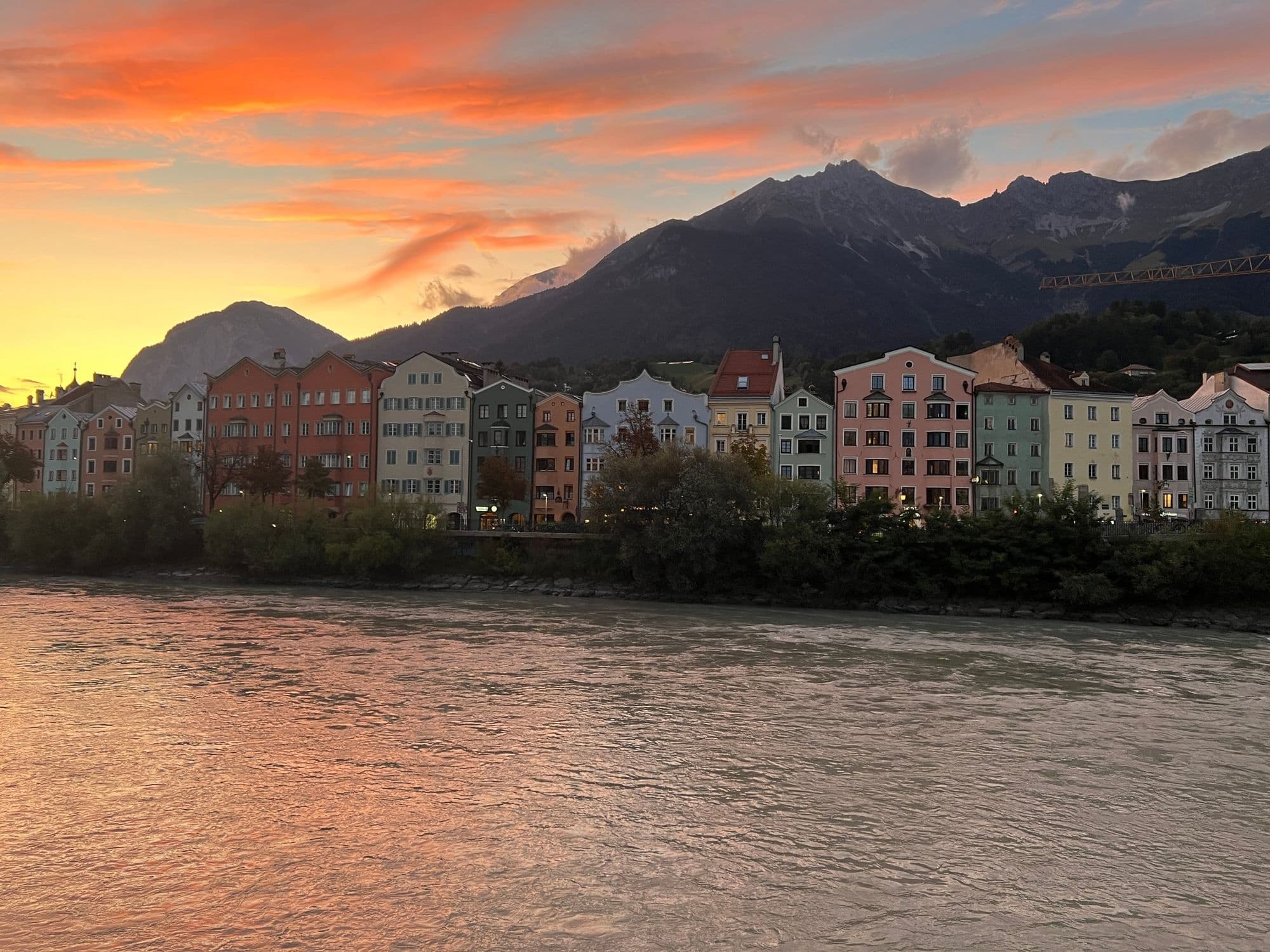 Colourful houses along the Inn river under an orange sunset sky