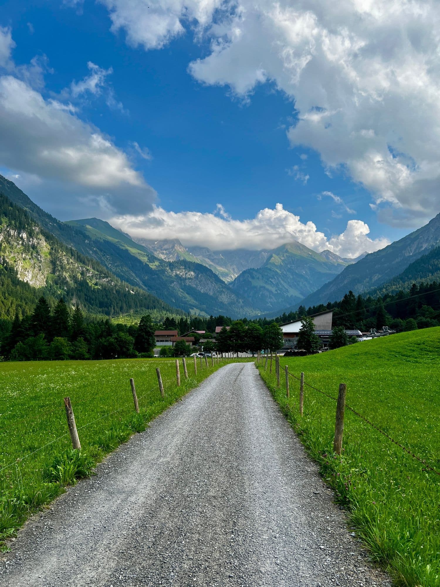 Gravel path between green meadows leading to the Allgäu Alps under big clouds